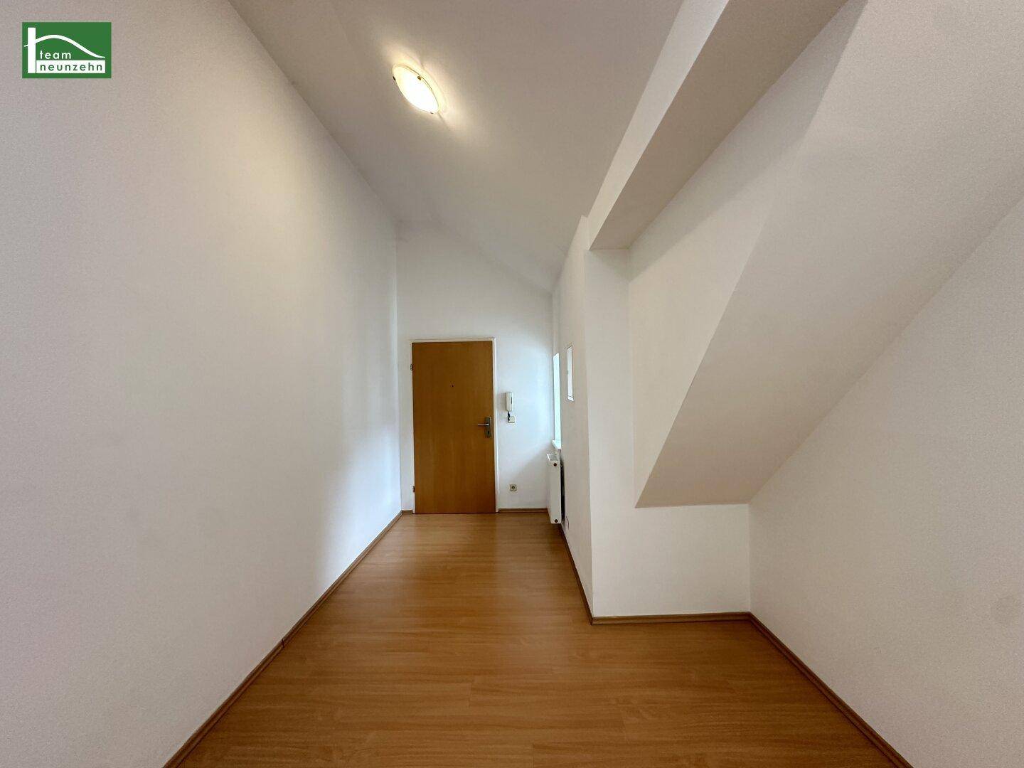 Eingangsbereich mit Laminatboden, weiß gestrichenen Wänden und einer Holztür.