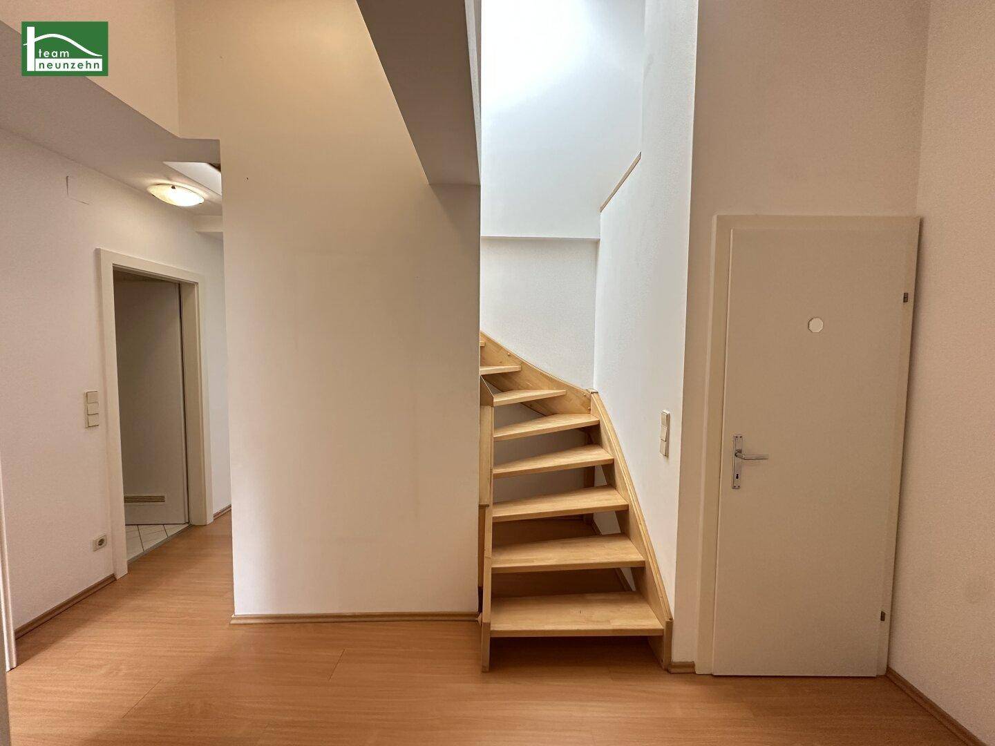 Flur mit Laminatboden und einer offenen Holztreppe, die zu den oberen Etagen führt.