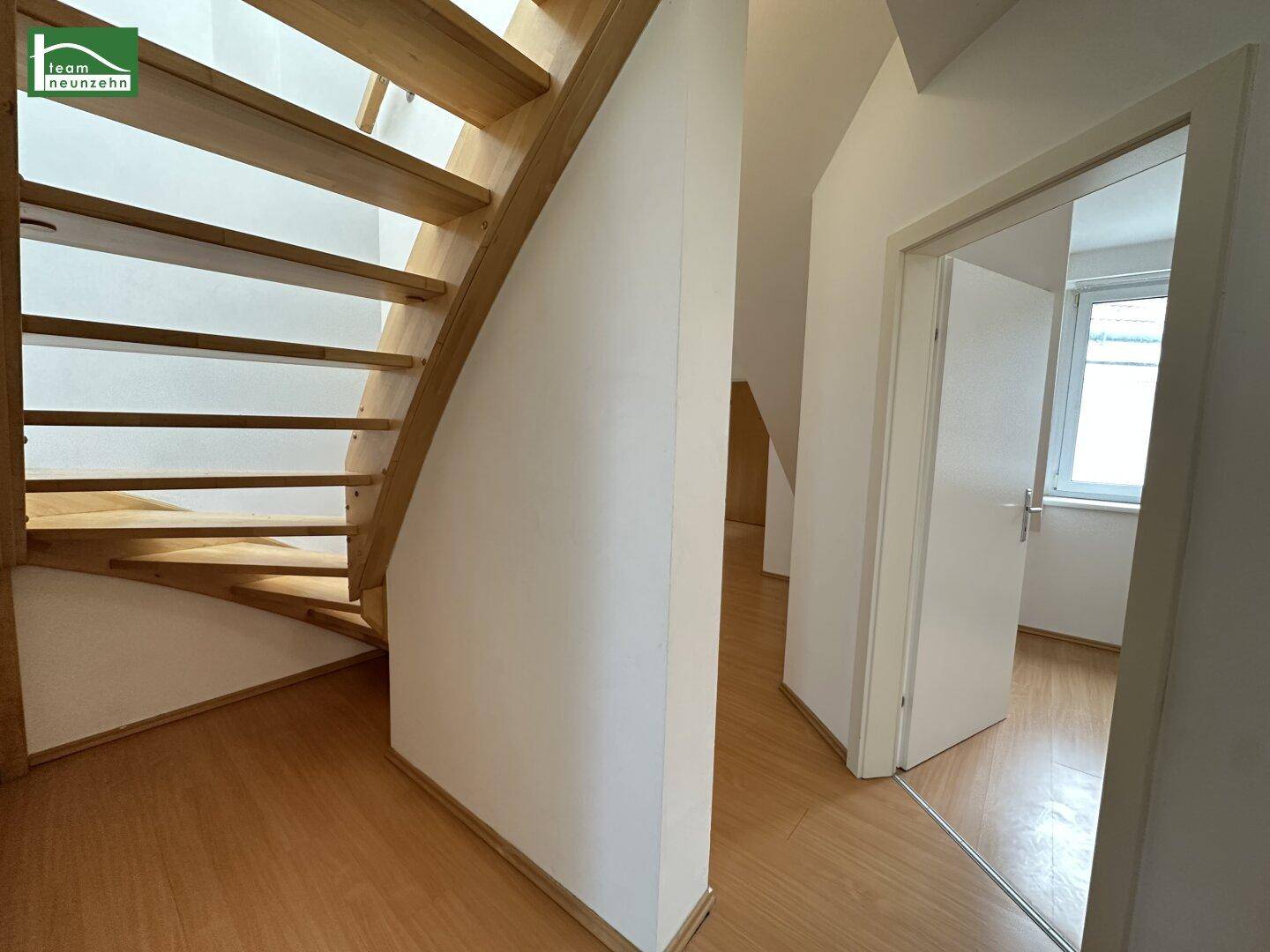 Detailansicht einer Holztreppe im Flur mit Laminatboden und weiß gestrichenen Wänden.
