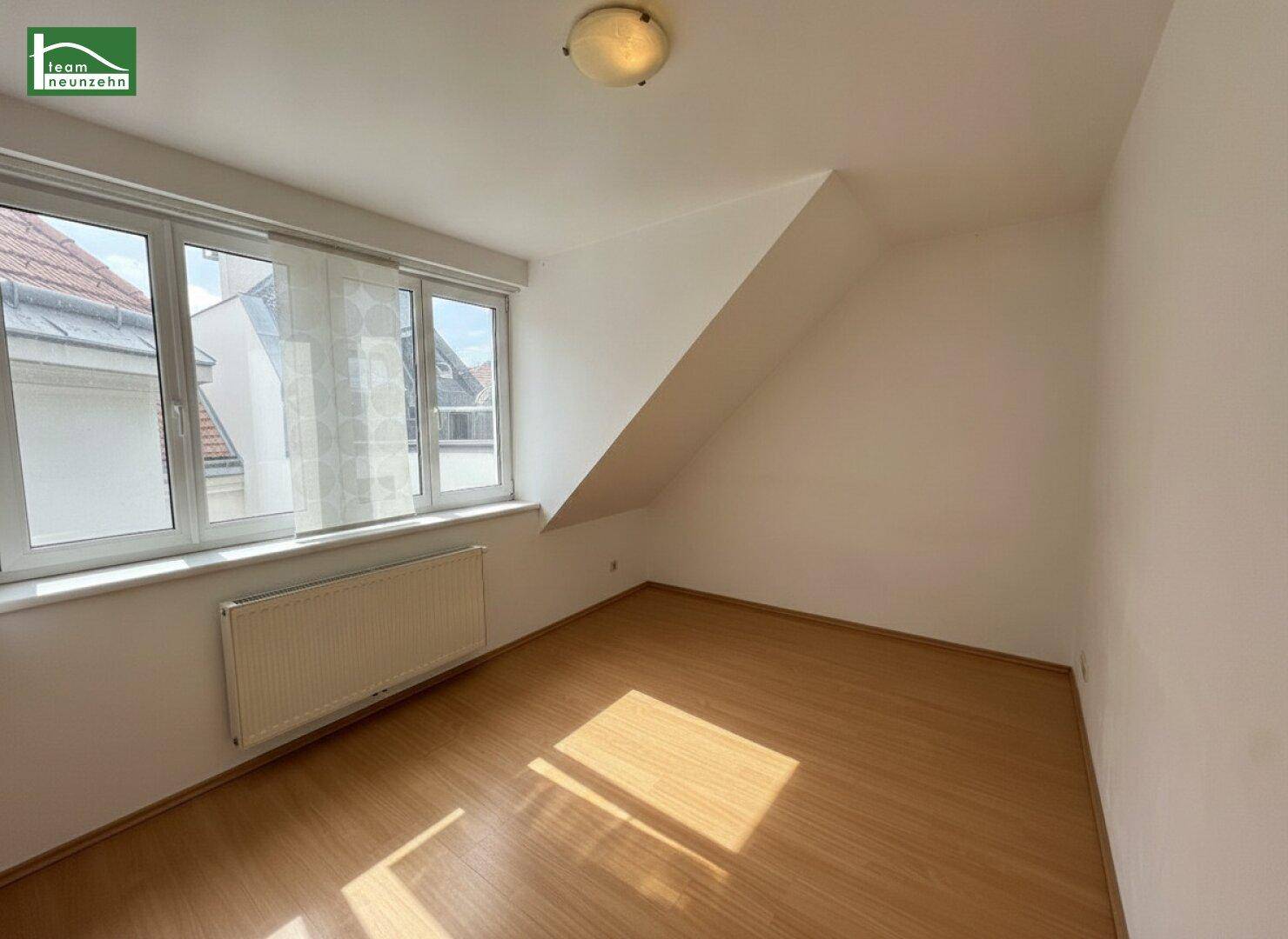 Helles Zimmer im Dachgeschoss mit Laminatboden, großem Fenster und schräger Wand.