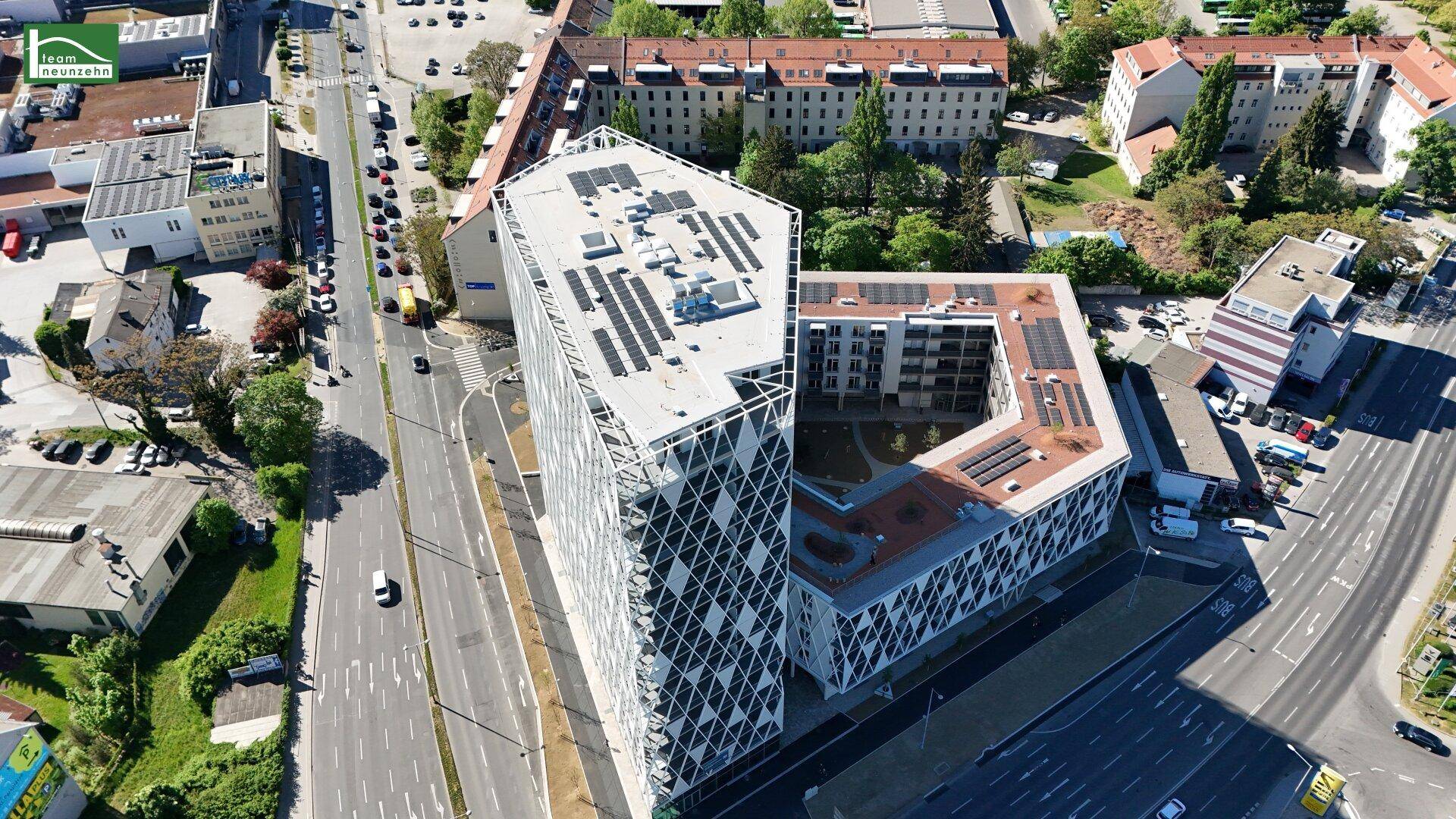 Luftaufnahme eines modernen Gebäudekomplexes mit markanter geometrischer Fassade und Solaranlagen auf dem Dach.