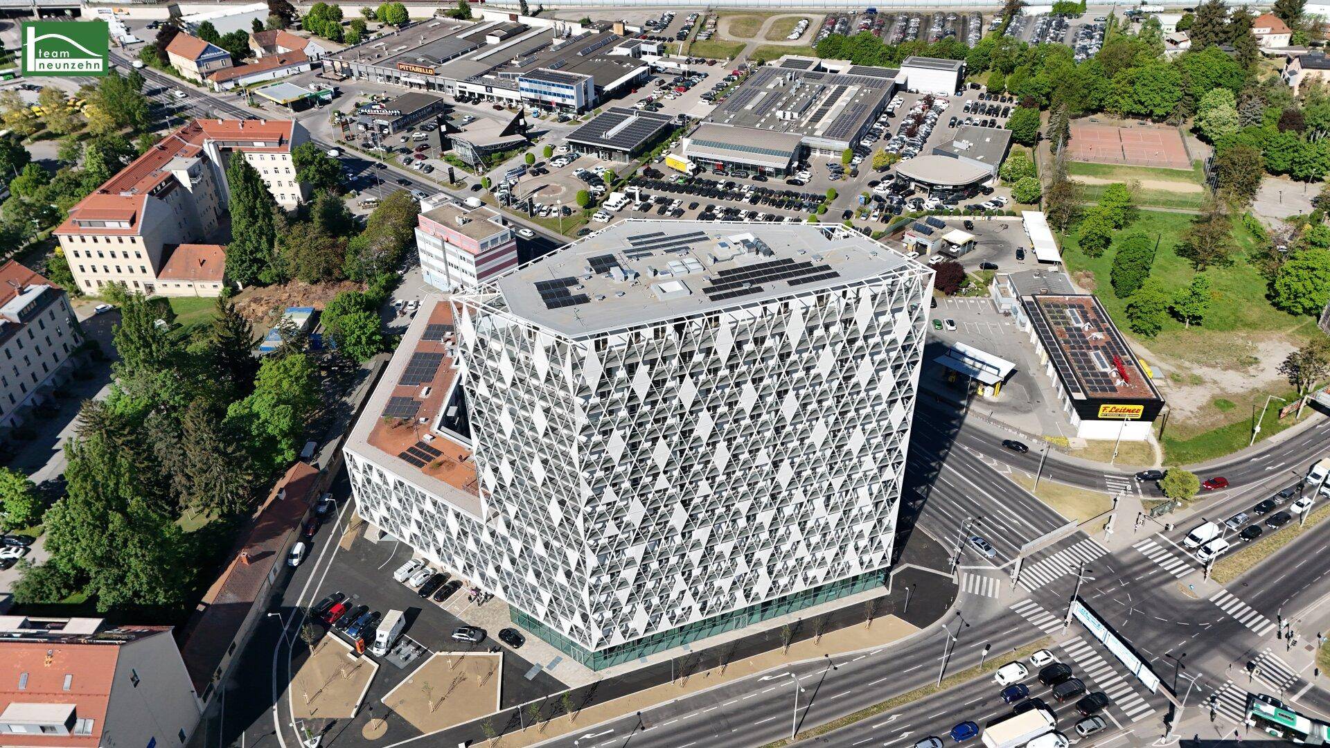 Luftaufnahme eines modernen Gebäudes mit markanter geometrischer Fassade und Solaranlagen auf dem Dach in städtischer Umgebung.