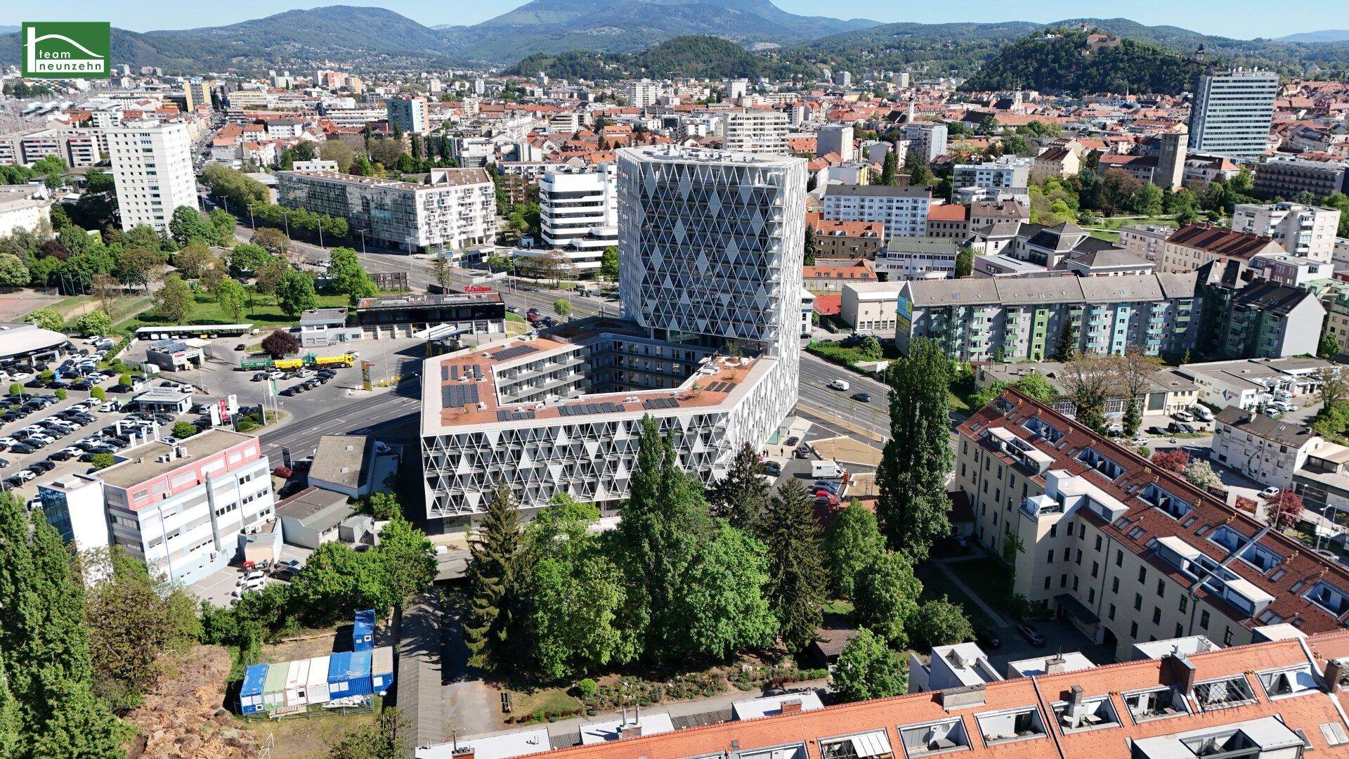 Panoramablick aus der Luft auf ein modernes Gebäude in der Stadt mit Bergen im Hintergrund.