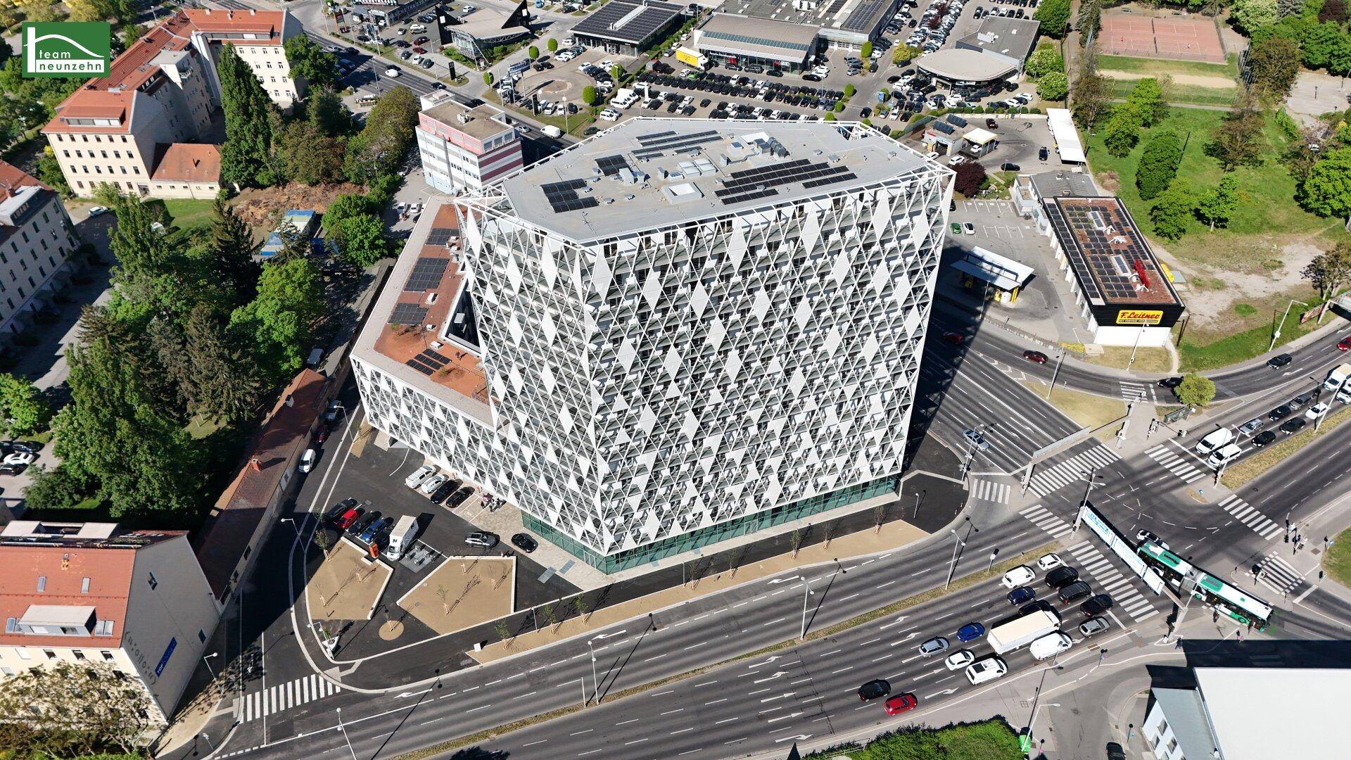 Luftaufnahme eines modernen Gebäudekomplexes mit markanter Fassade in städtischer Umgebung.