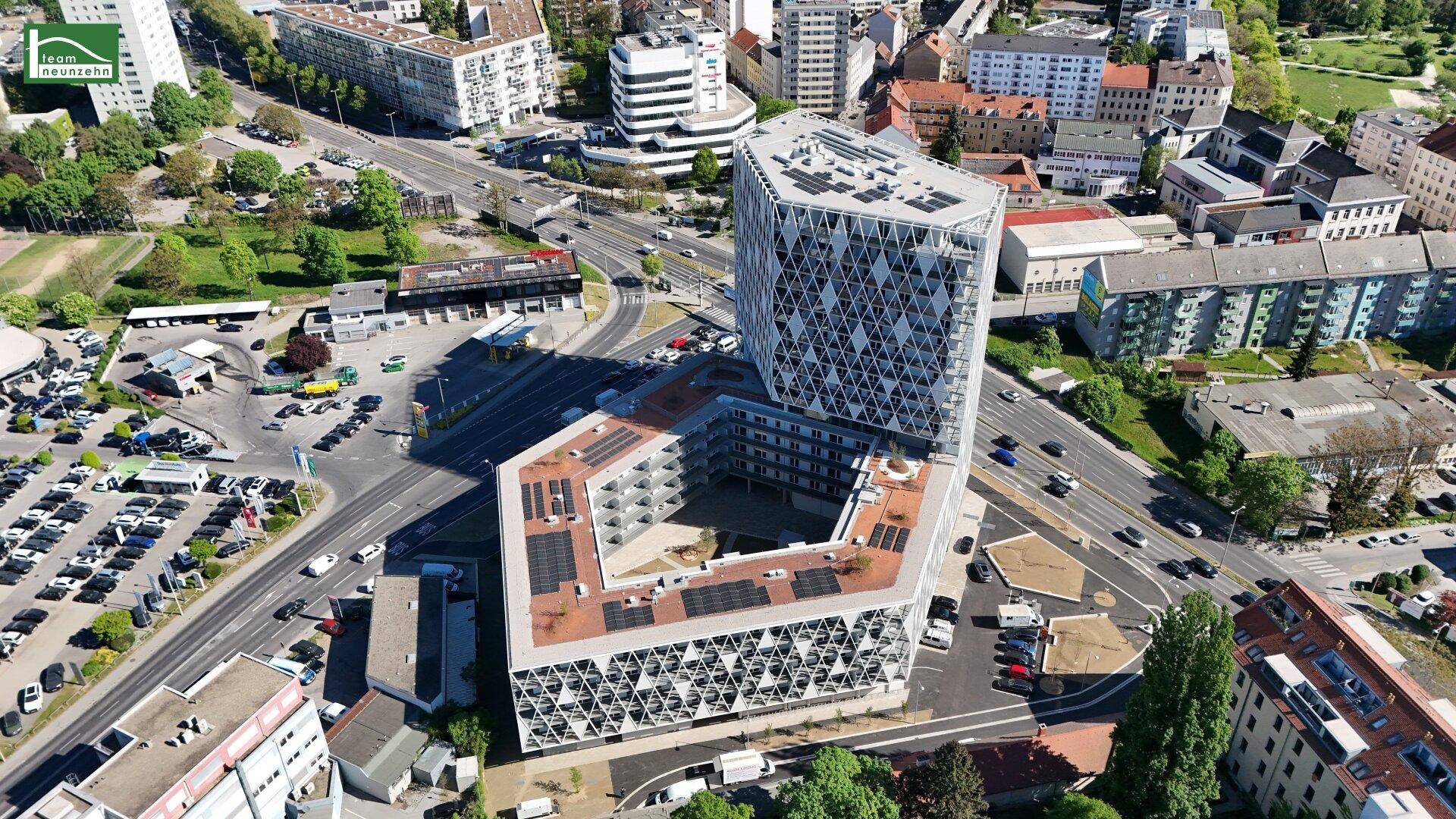 Luftaufnahme eines modernen Gebäudekomplexes mit markanter Fassade, Solaranlagen und städtischer Umgebung.