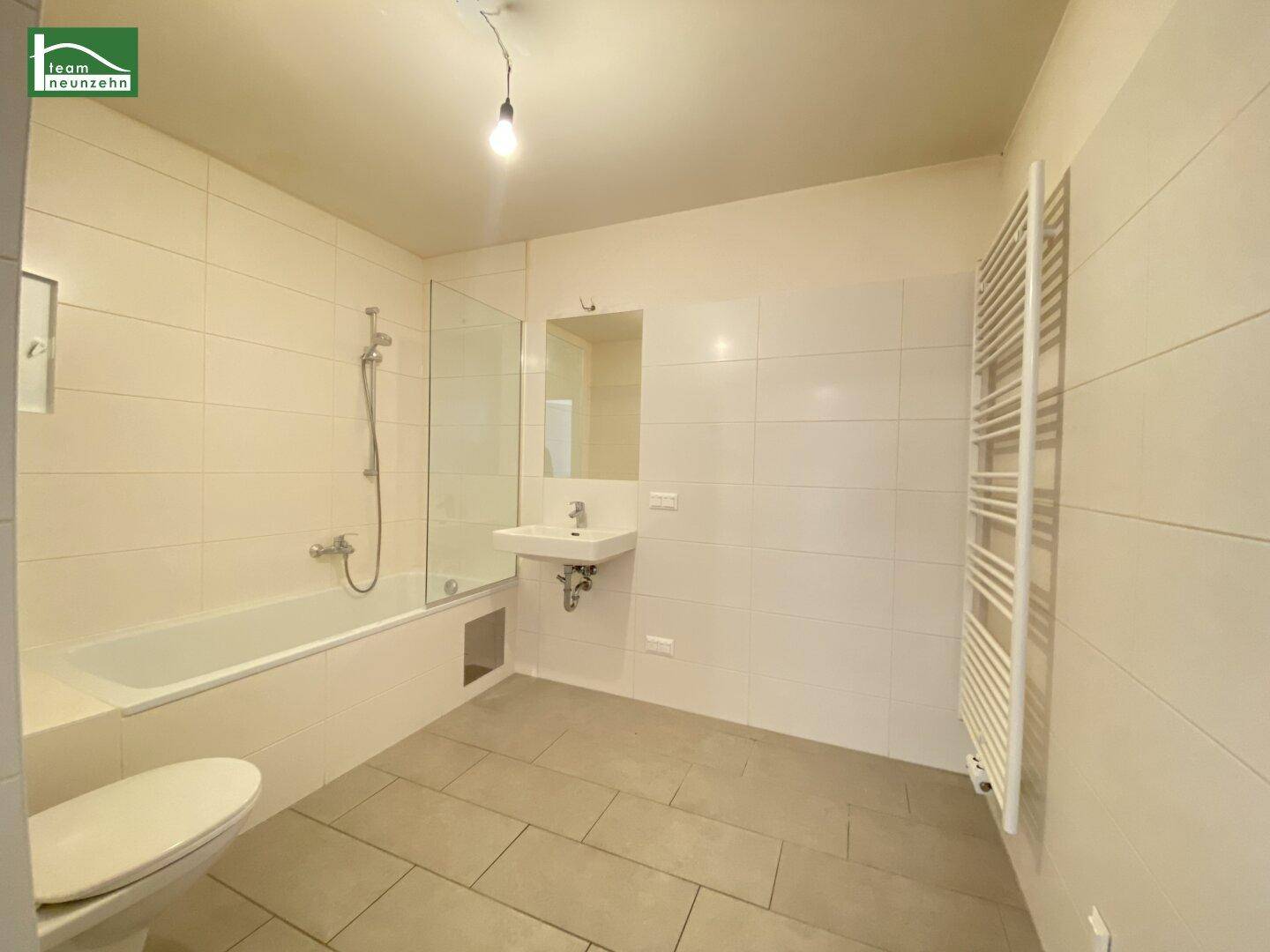 Modernes Badezimmer mit weißen Fliesen, Badewanne mit Duschfunktion und beheiztem Handtuchhalter.