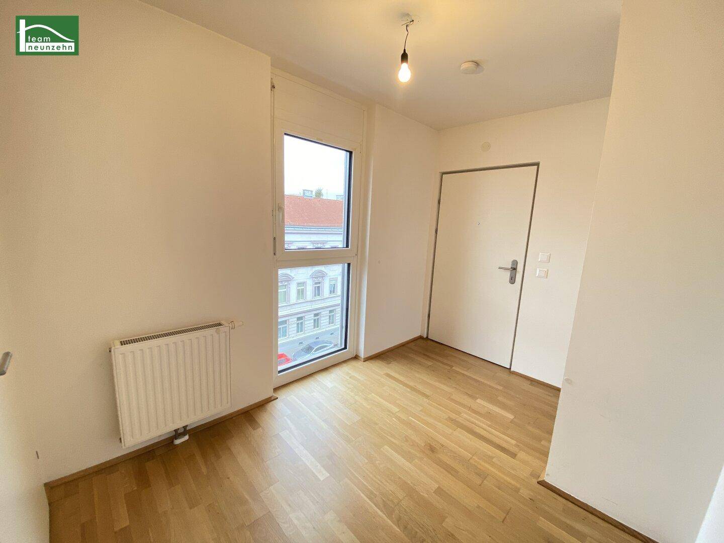 Heller Eingangsbereich mit Parkettboden, Fenster und Zugang zur Wohnungstür.