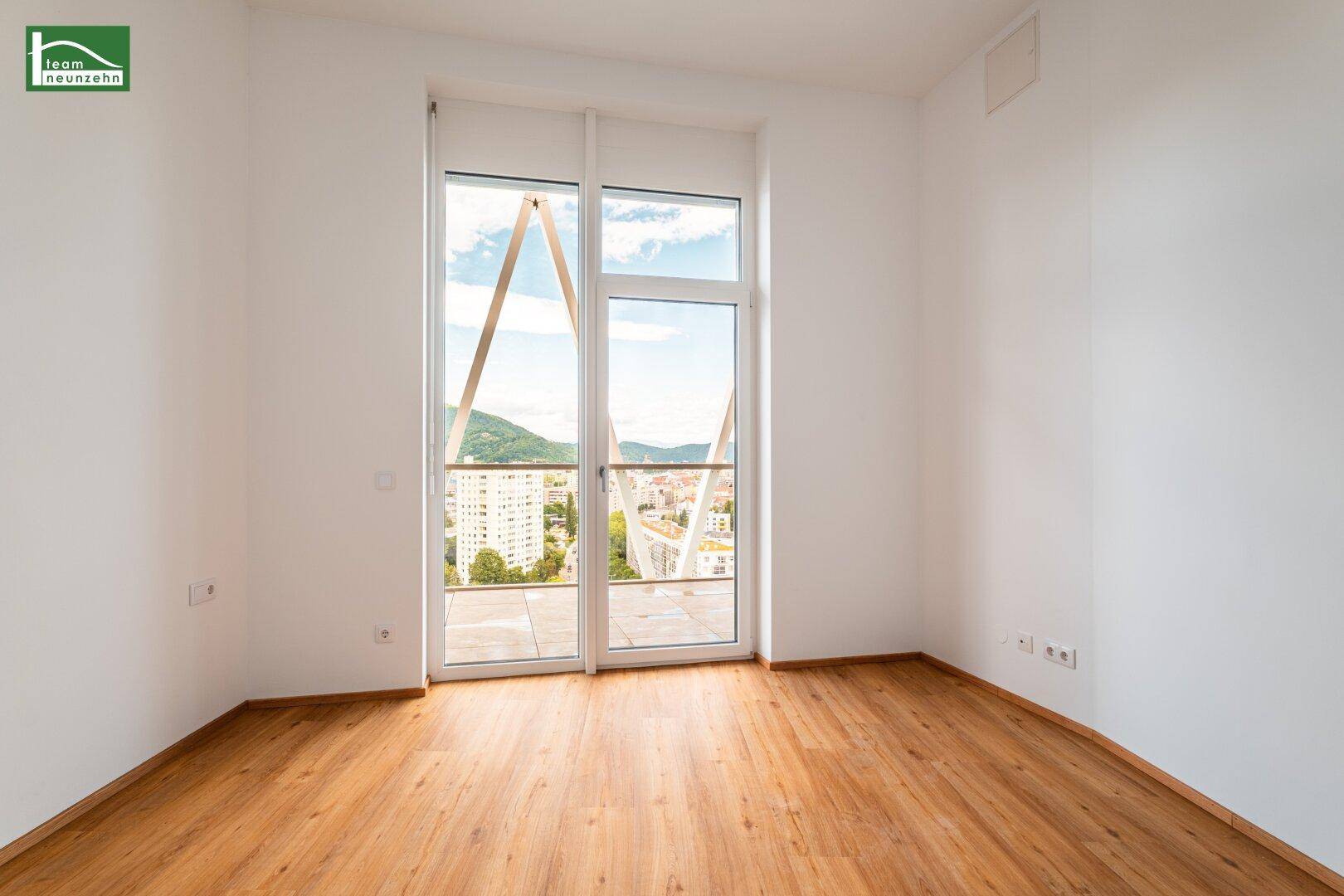 Helles Schlafzimmer mit Holzboden und Zugang zu einem Balkon mit Panoramablick über die Stadt.