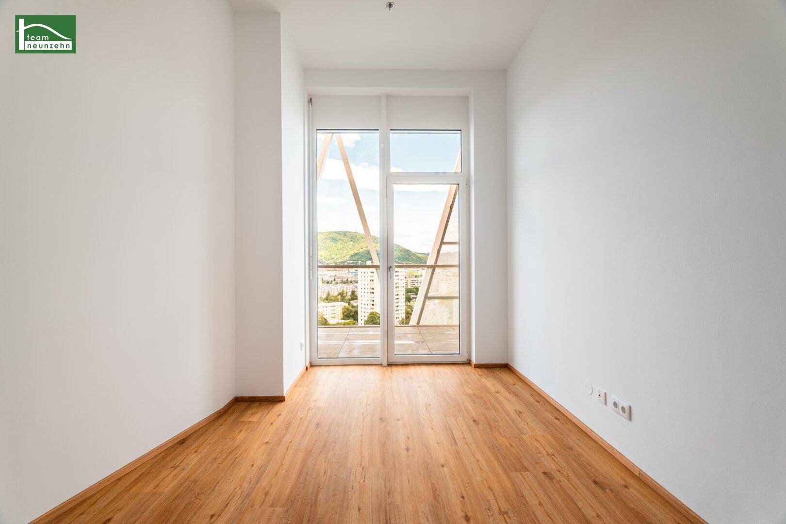 Helles Zimmer mit Holzboden und großen Fenstern, die einen weiten Blick auf die Umgebung bieten.