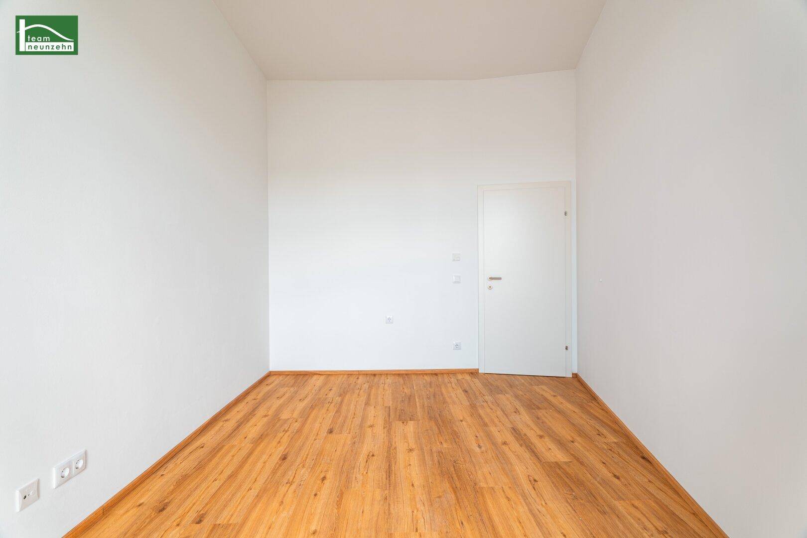 Leeres Zimmer mit Holzboden und weiß gestrichenen Wänden, ideal für ein Gästezimmer oder Büro.