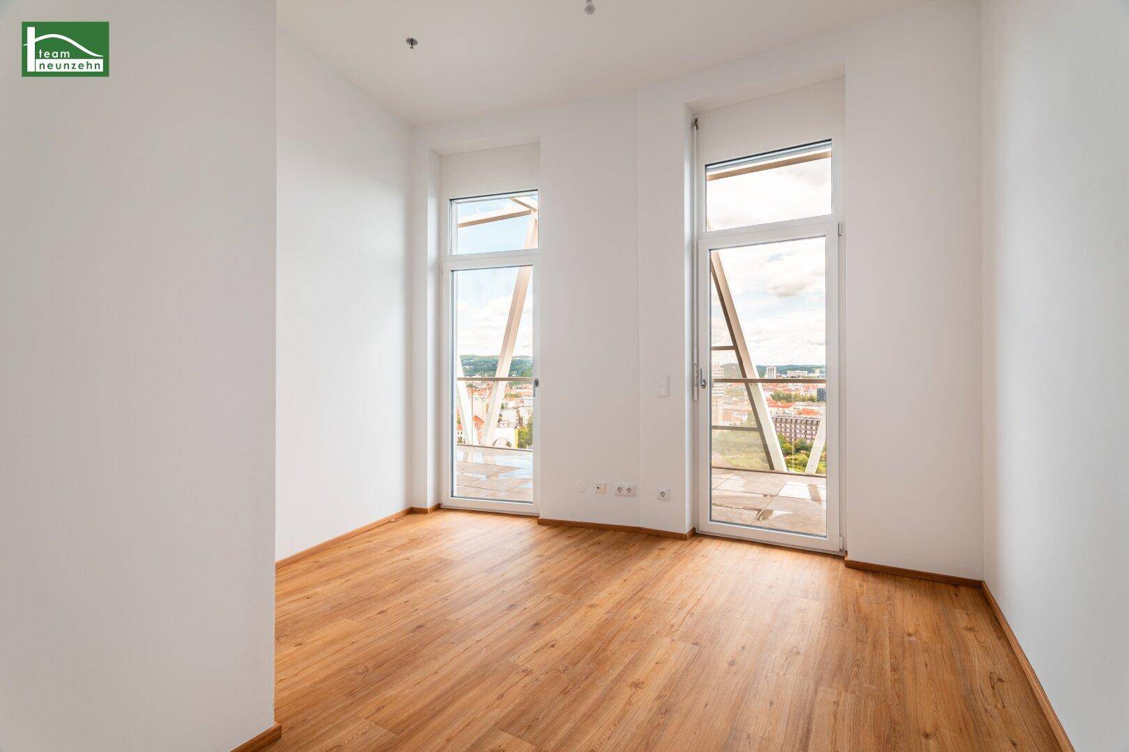 Geräumiges Zimmer mit Holzboden und zwei großen Fenstern mit weitem Stadtblick.