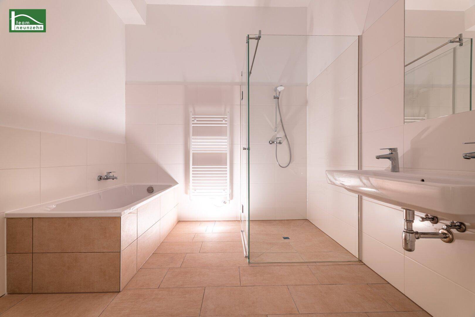 Helles Badezimmer mit Badewanne, Dusche, Waschbecken und beheiztem Handtuchhalter.