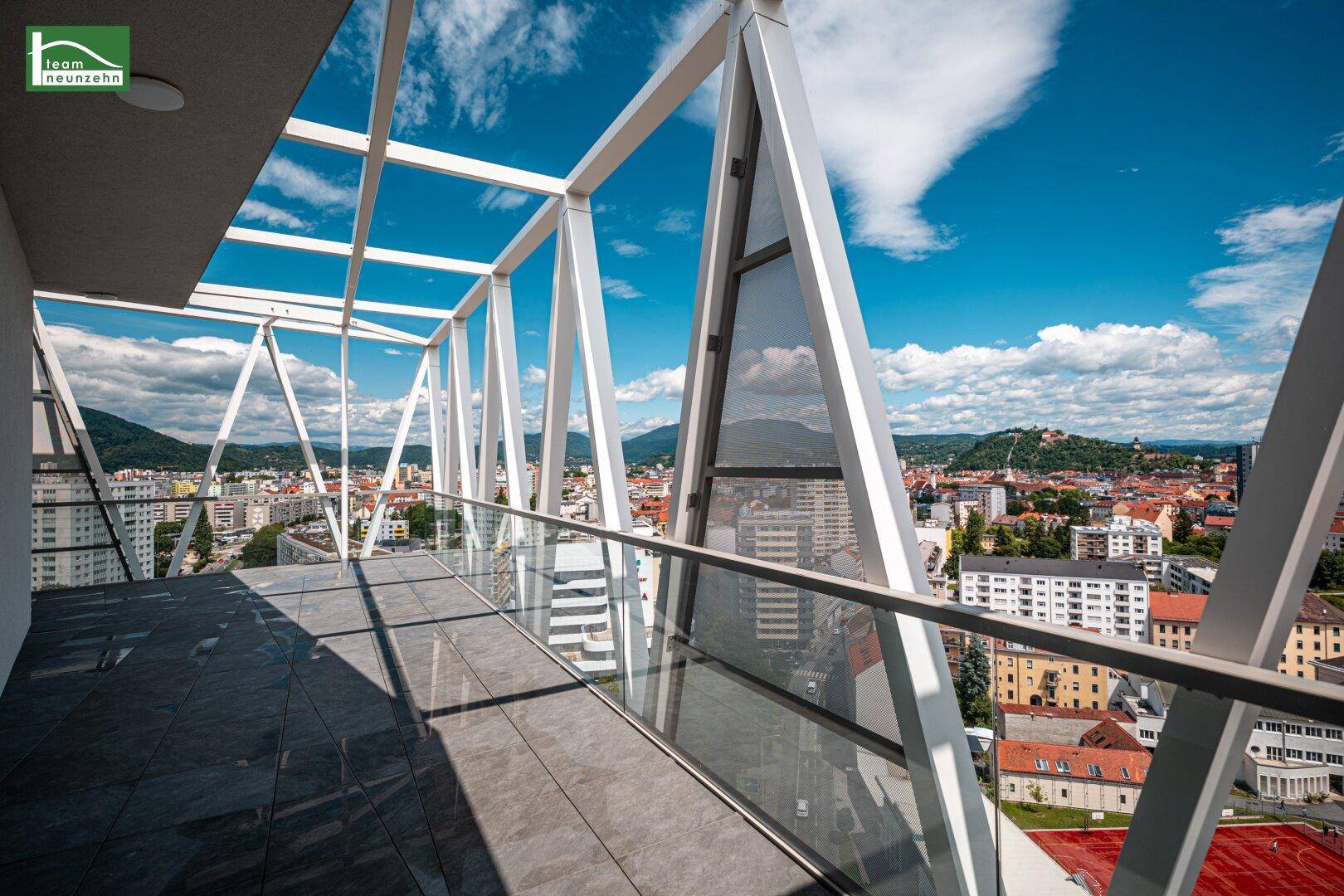 Großer Balkon mit moderner Glasbrüstung und weitem Blick über die Stadt unter blauem Himmel.