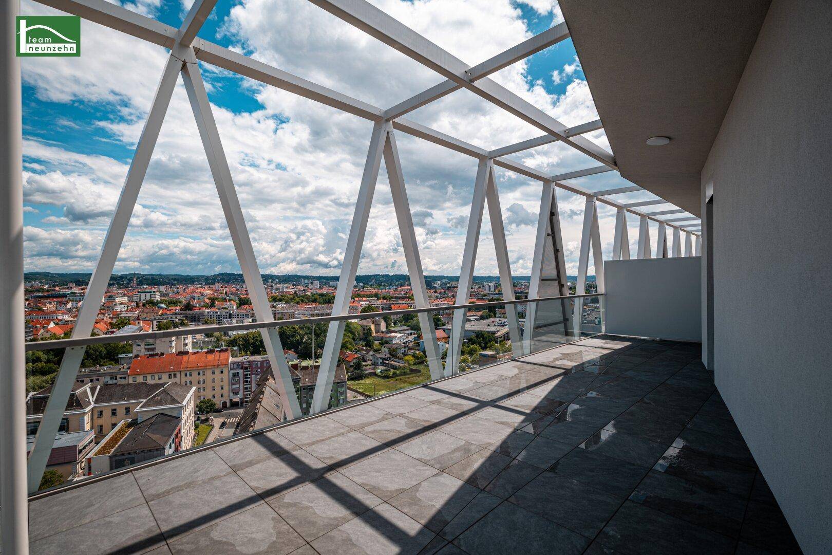 Geräumiger Balkon mit Fliesenboden und offener Stahlkonstruktion, bietet Panoramablick auf die Stadt.