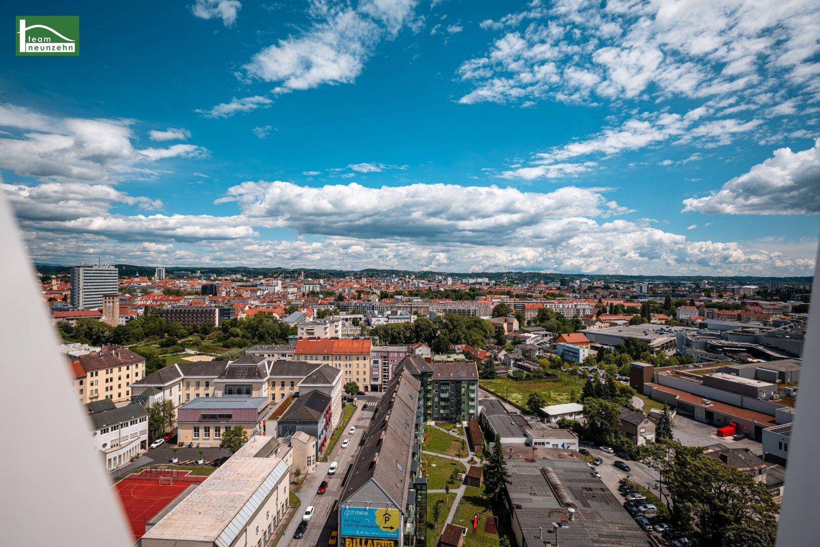 Panoramablick über die Stadt mit Wohngebäuden und grünen Flächen unter blauem Himmel.