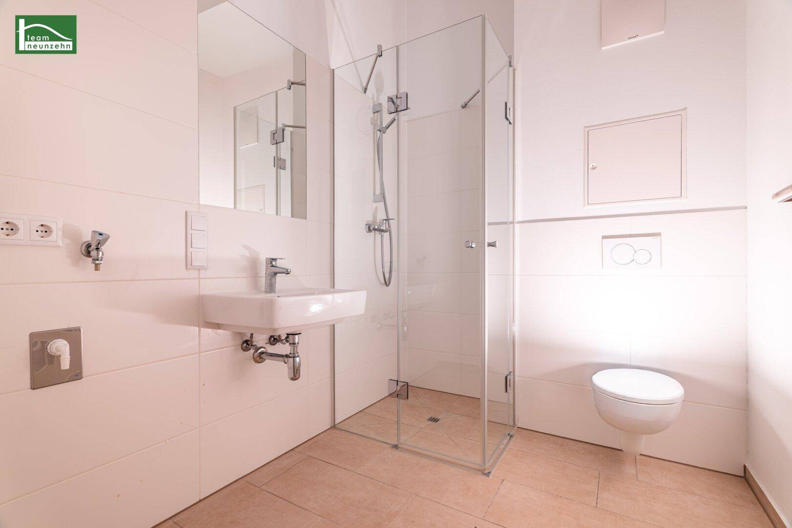 Modernes Badezimmer mit ebenerdiger Dusche, wandhängendem WC und hellem Fliesenboden.