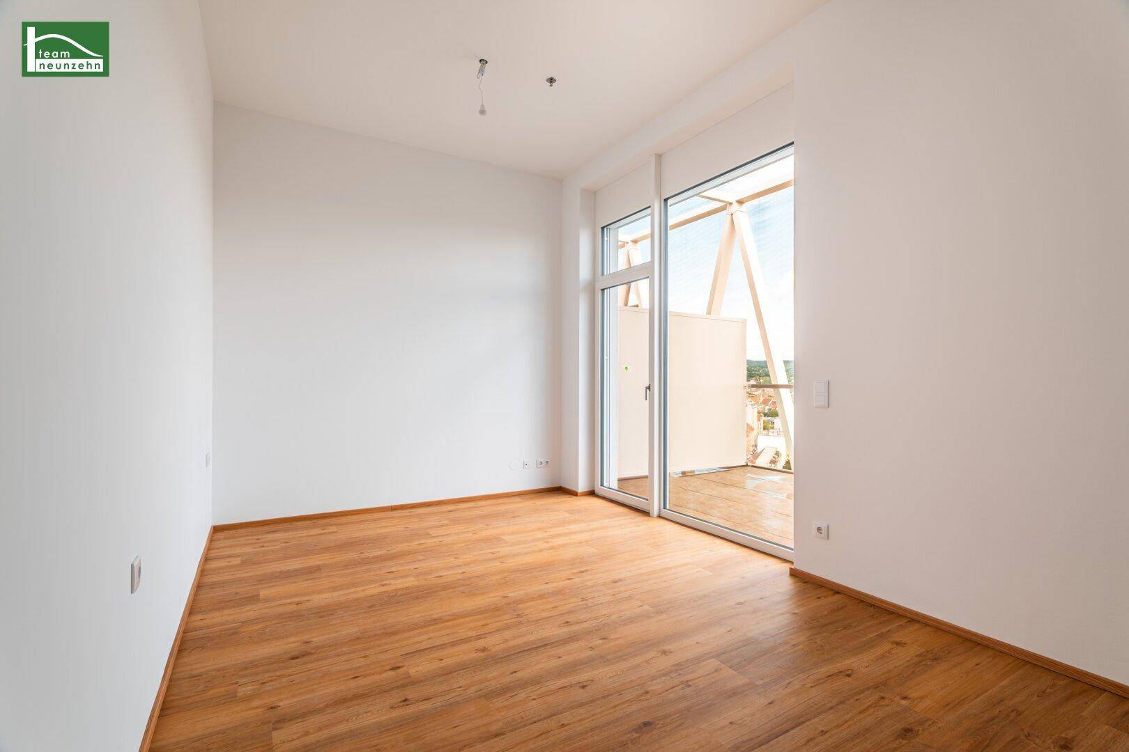 Heller Raum mit Holzboden und Zugang zu einem Balkon mit Stadtblick.