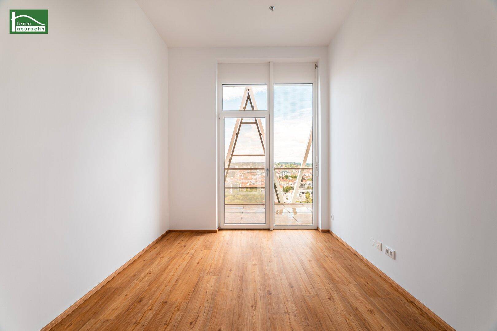 Heller Raum mit Holzboden und bodentiefen Fenstern, die einen weiten Blick bieten.