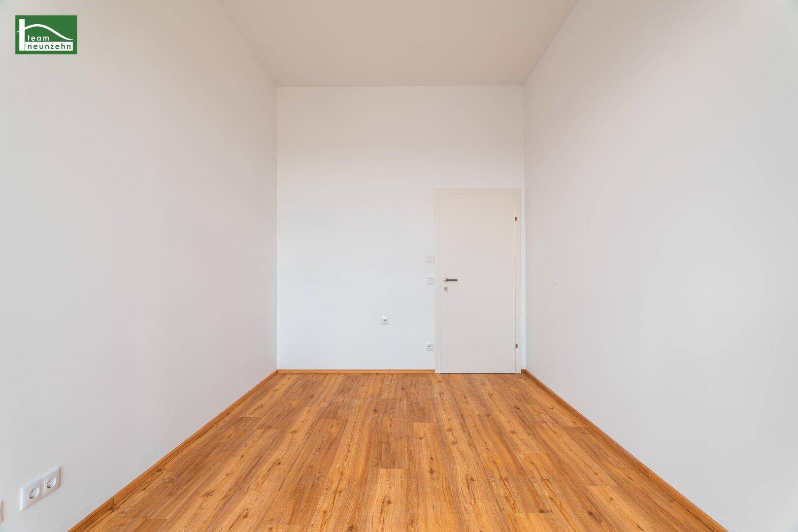 Leerer Raum mit Holzboden und einer schlichten weißen Tür, bereit zur individuellen Gestaltung.