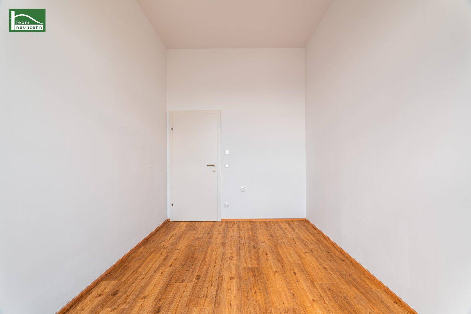 Schlichter, leerer Raum mit Holzboden und einer weißen Tür, ideal für verschiedene Nutzungen.