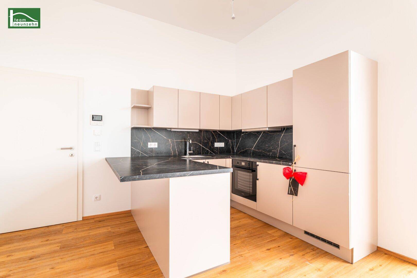 Moderne Einbauküche mit beigen Fronten, dunkler Arbeitsplatte und integriertem Backofen.