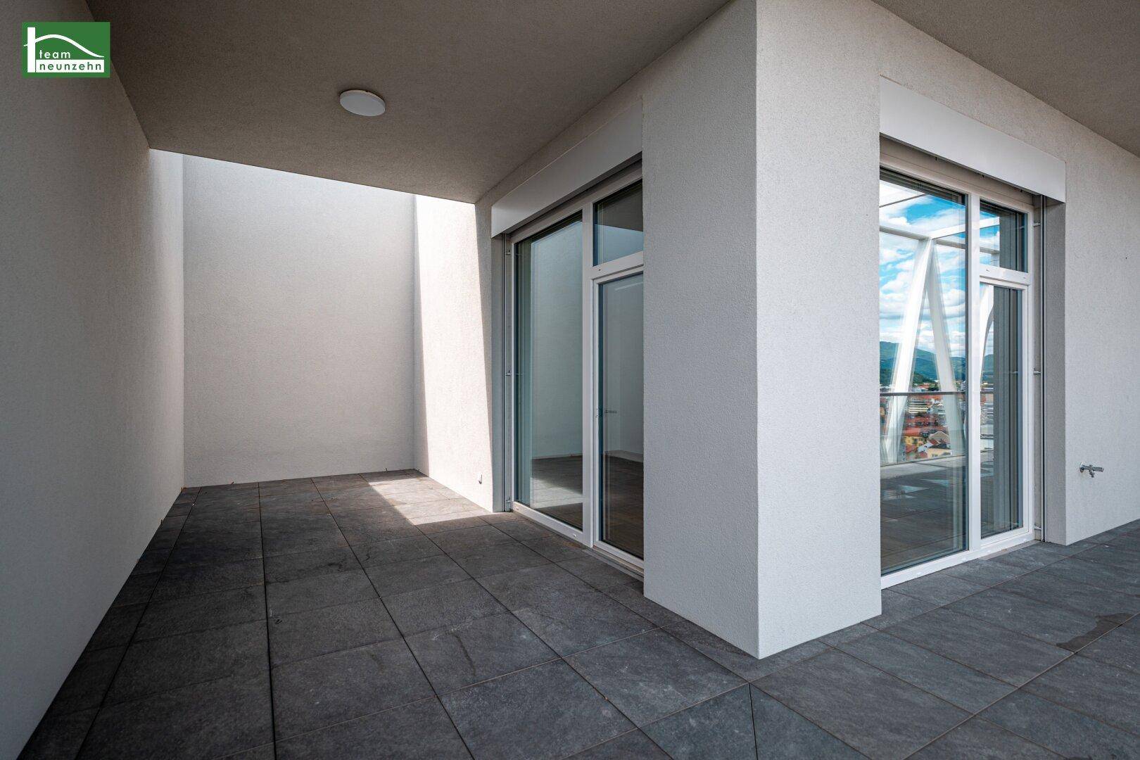 Überdachte Loggia mit dunklen Fliesen und viel Tageslicht, ideal zum Entspannen.