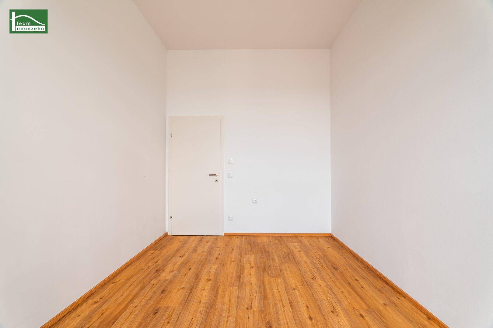 Leerer Raum mit Laminatboden und einer schlichten weißen Tür, bereit zur individuellen Gestaltung.