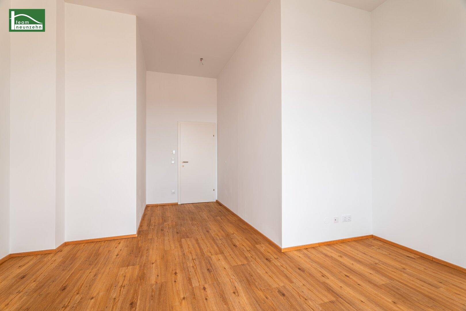 Schlichter, leerer Raum mit Laminatboden und einer Tür, bereit für die Einrichtung nach Wunsch.