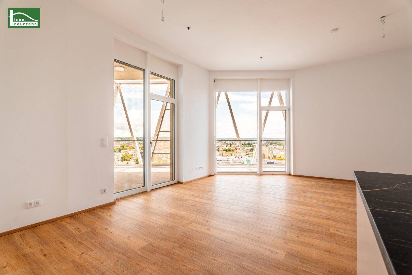 Großzügiges Wohnzimmer mit Laminatboden und zwei Balkonzugängen, die einen weiten Stadtblick ermöglichen.