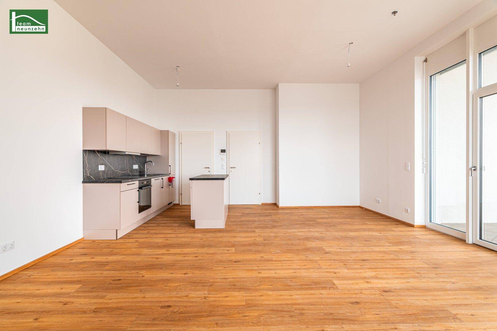Moderne Einbauküche in einem offenen Wohnbereich mit Laminatboden und viel Tageslicht.