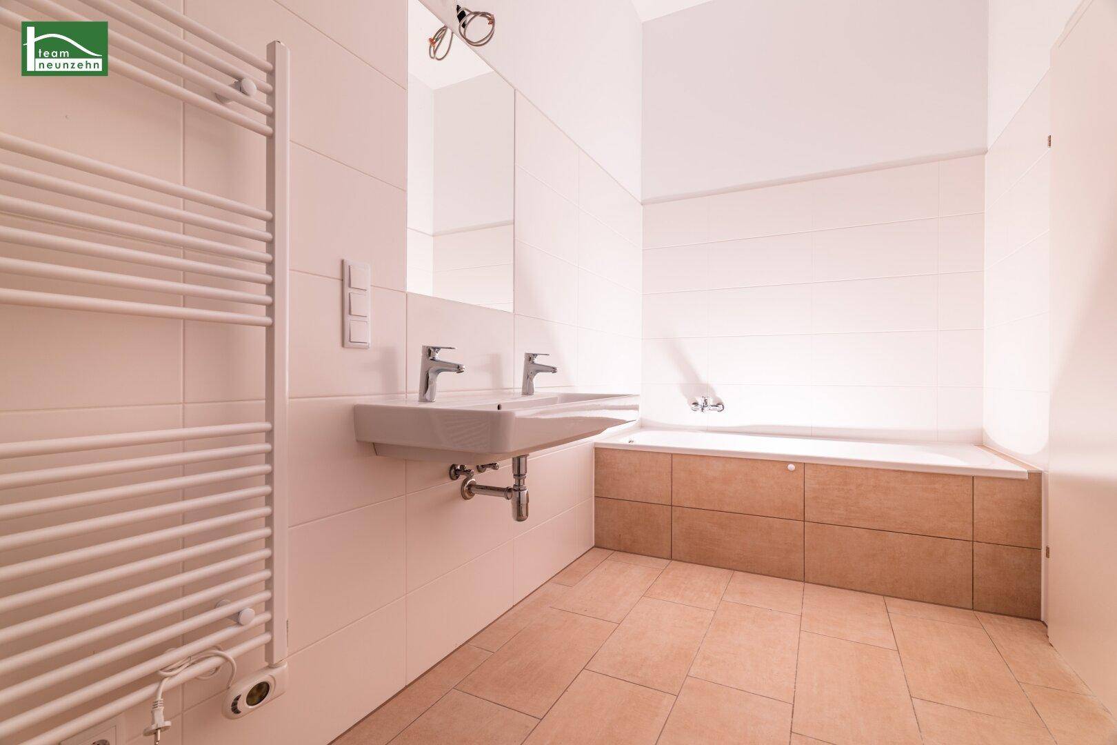 Helles Badezimmer mit Badewanne, Doppelwaschbecken und modernem beheiztem Handtuchtrockner.