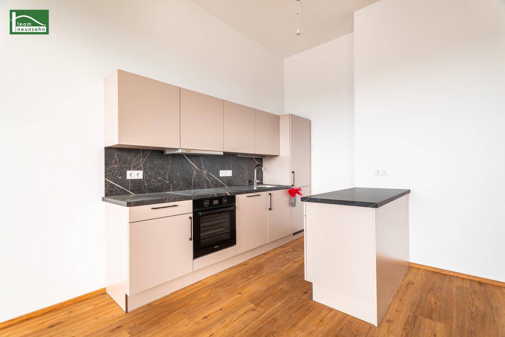 Moderne Einbauküche mit beigen Schränken, dunkler Arbeitsplatte und integrierten Geräten.
