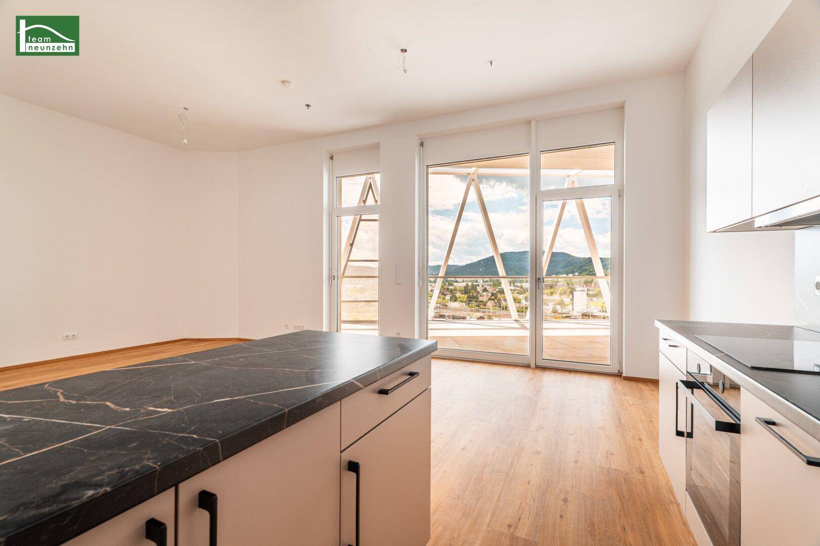Offener Wohnbereich mit Kücheninsel und weitem Blick über die Stadt und die umliegenden Berge.