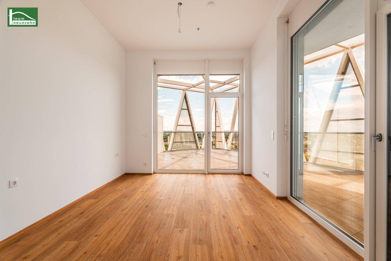 Helles Schlafzimmer mit Holzboden und großen Fenstern, die Zugang zu einem Balkon mit Aussicht bieten.