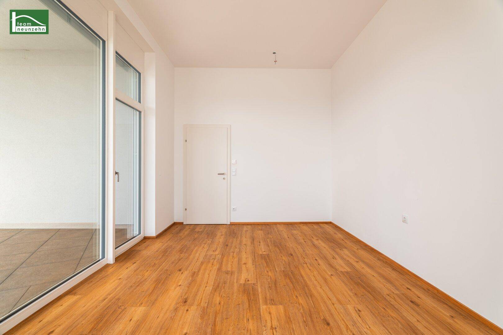 Leeres Zimmer mit Holzboden, weißen Wänden und einer Tür, bereit zur individuellen Gestaltung.