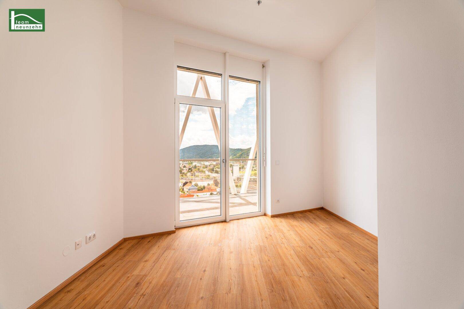 Geräumiges Zimmer mit Holzboden und großen Fenstern, die einen weiten Blick auf die Umgebung ermöglichen.