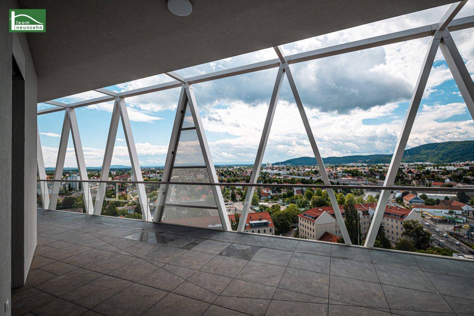Geräumiger Balkon mit Fliesenboden, Glasgeländer und beeindruckendem Panoramablick über die Stadt und Berge.