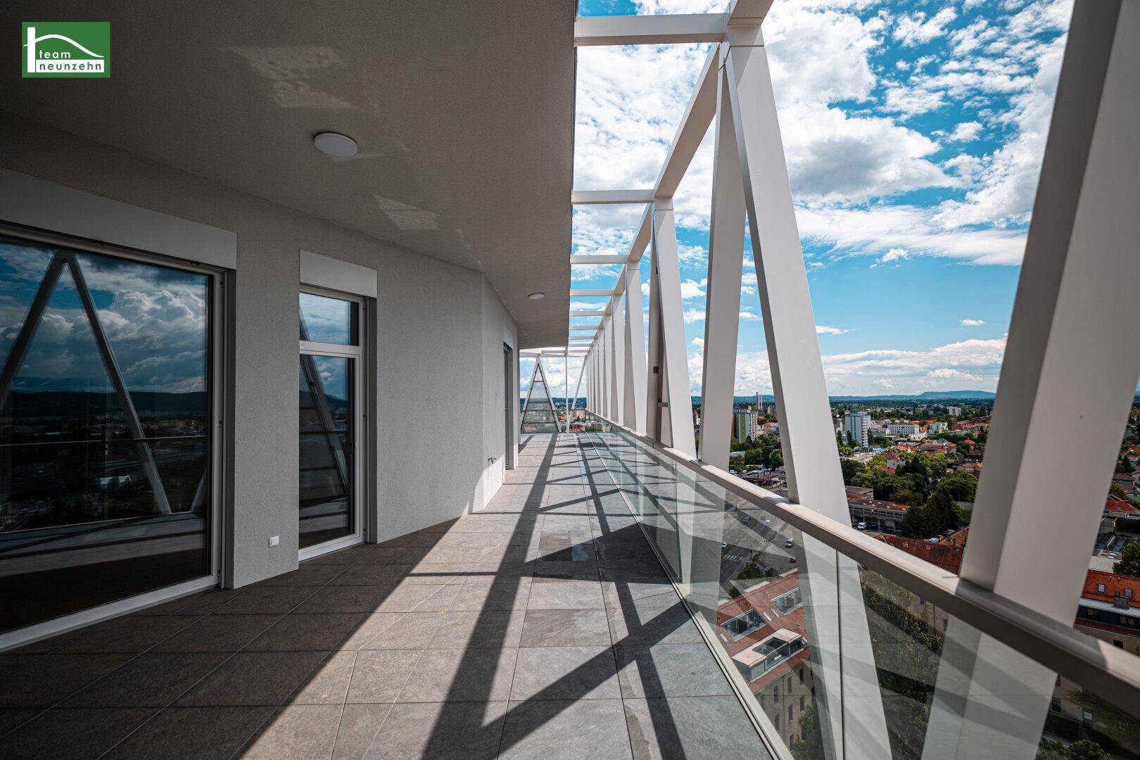 Langer Balkon mit moderner Glasbrüstung, geometrischer Struktur und weitem Stadtblick.