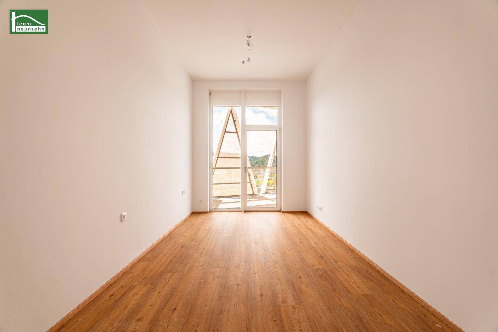 Heller, leerer Raum mit Holzboden und Zugang zu einem Balkon mit Bergblick.