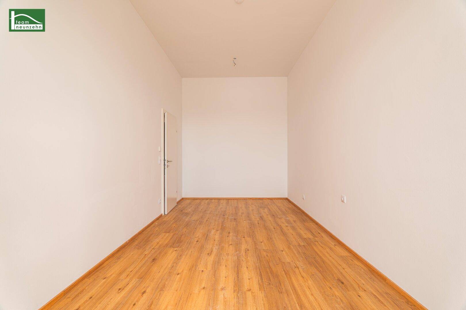 Geräumiger, unmöblierter Raum mit Holzboden und einer weißen Tür, ideal für verschiedene Nutzungen.