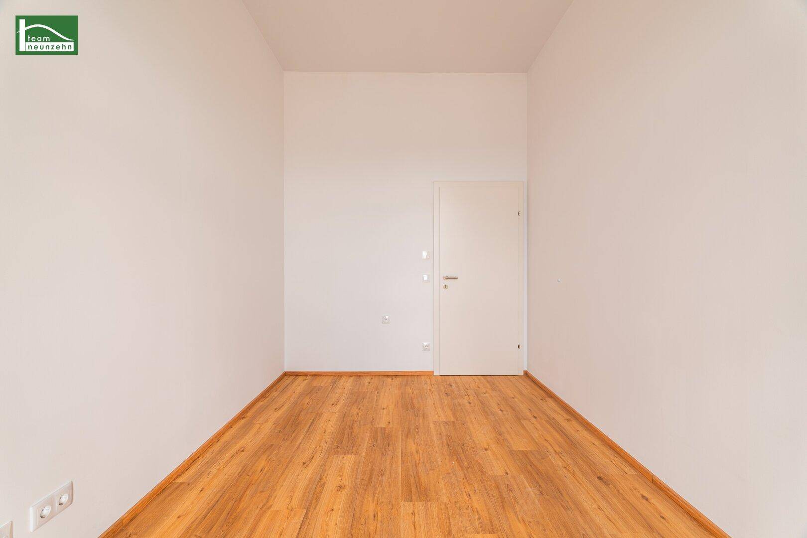 Unmöblierter Raum mit Holzboden und einer schlichten weißen Tür, bereit für neue Bewohner.