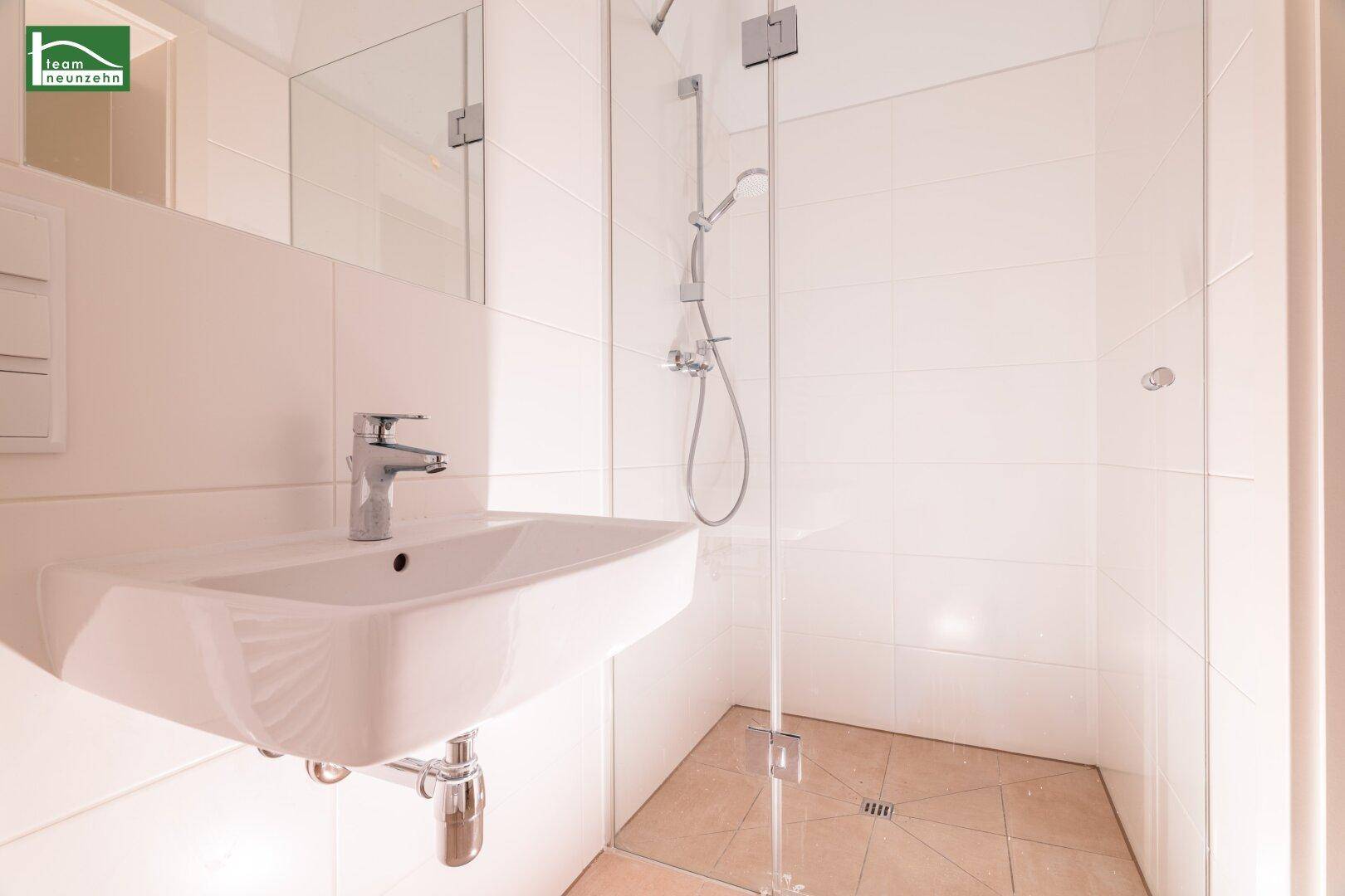Modernes Badezimmer mit weißen Fliesen, Einzelwaschbecken und einer begehbaren Dusche mit Glaswand.