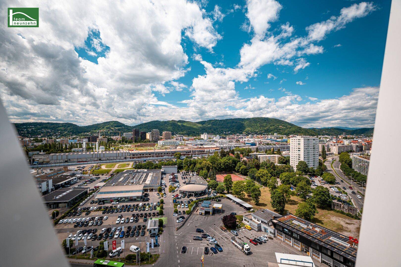 Weitläufiger Panoramablick über die Stadt, Industriegebiete und die umliegende Berglandschaft unter blauem Himmel.