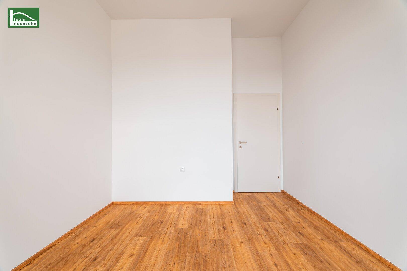 Unmöblierter Raum mit Holzboden und weißer Tür, ideal für verschiedene Nutzungsmöglichkeiten.