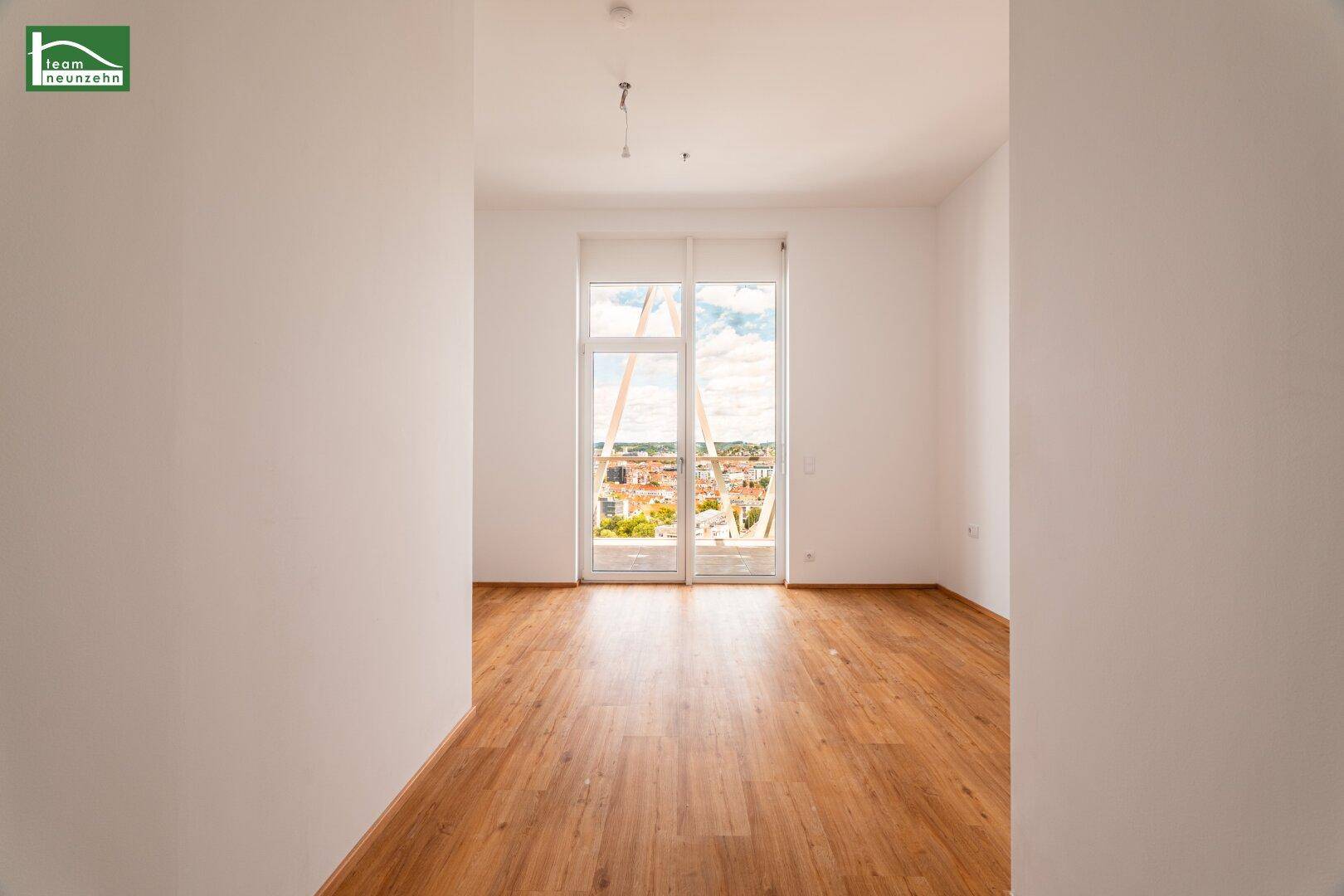 Lichtdurchfluteter Raum mit Holzboden und weitem Blick auf die städtische Umgebung.