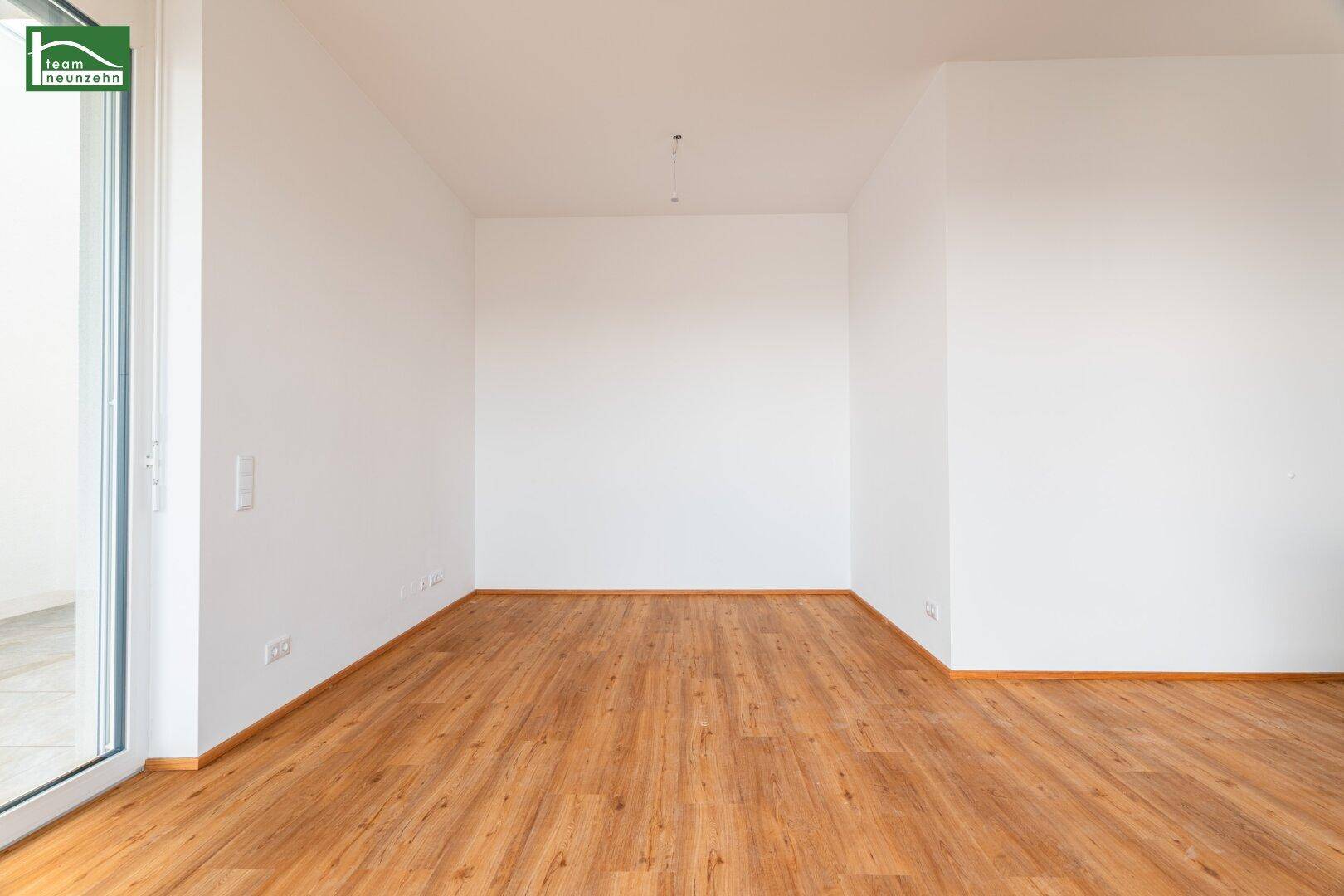 Heller, unmöblierter Raum mit Holzboden und großen Fenstern, die viel Licht hereinlassen.