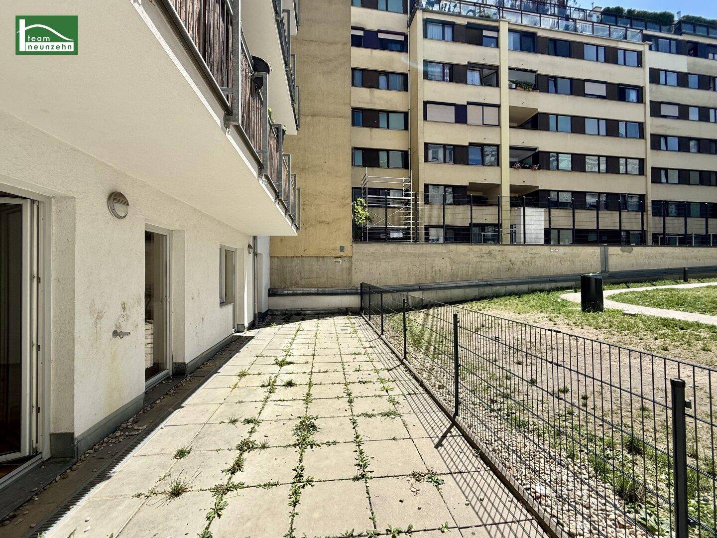 Große gepflasterte Terrasse neben dem Gebäude, mit Blick auf eine Grünfläche.