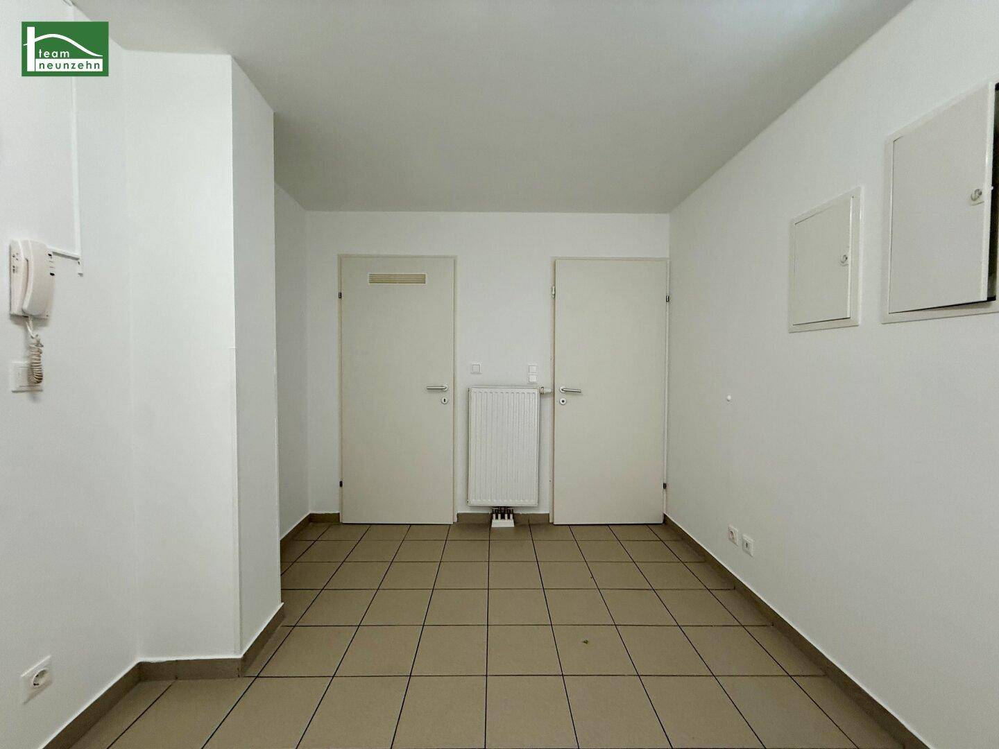 Eingangsbereich mit Fliesenboden, weißen Wänden und Gegensprechanlage.