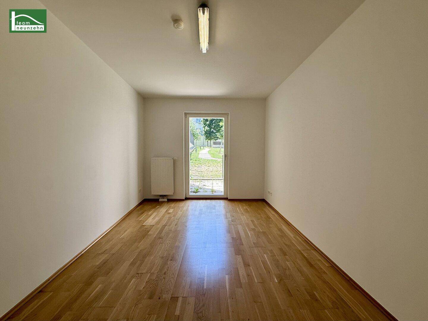 Geräumiges, unmöbliertes Zimmer mit Holzboden und direktem Zugang zum Garten.