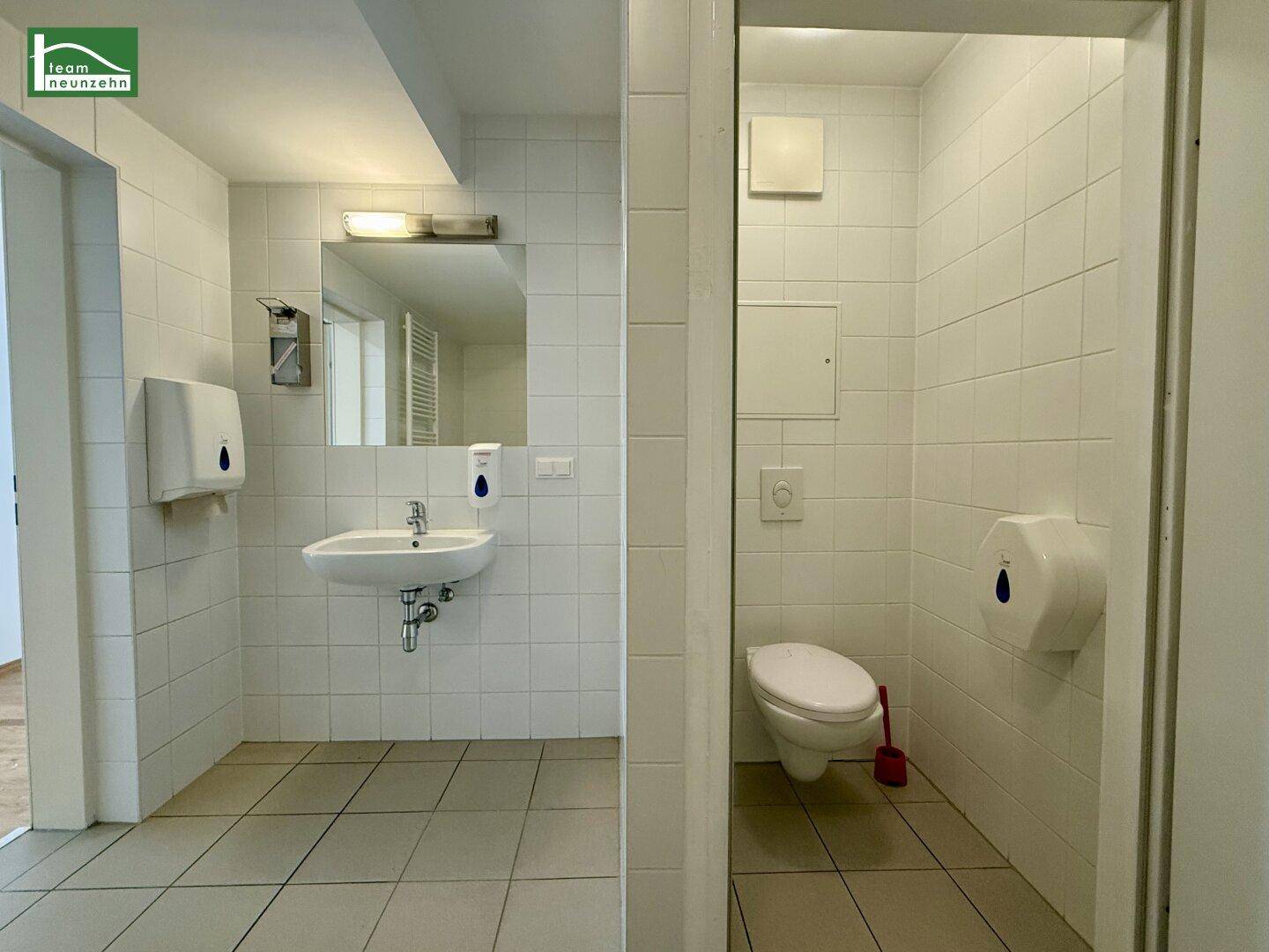 Helles Badezimmer mit Waschbecken, Spiegel und separatem WC-Bereich.